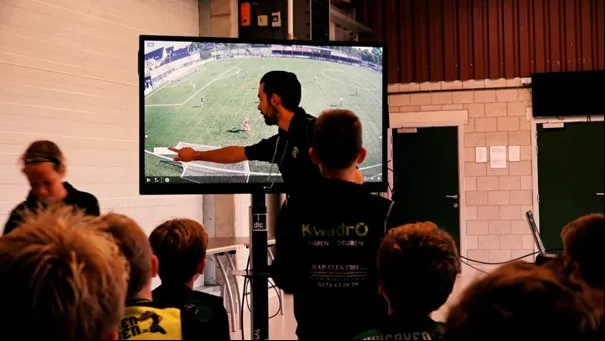 Een foto van een coach die tips geeft aan de voetballers via het tactics board.